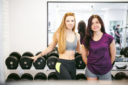 girl in a bright white gym. Two young sports women are chatting cutely near sports equipment about trenirovke with dumbbells. Healthy way of life, good spiritsの写真素材