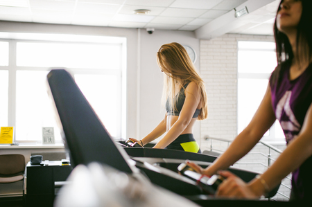 young woman is engaged fitness in gym. Performs cardio load on treadmill, running and walking with acceleration. sport, fit, lifestyle, technology and people conceptの写真素材