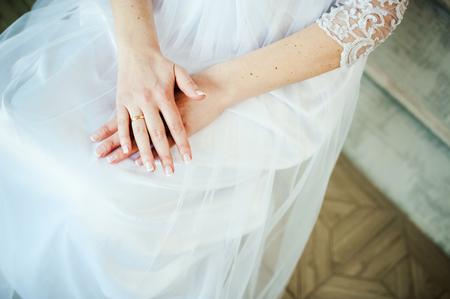 bride in a wedding dress folded her hands on her knees, an engagement ring on her fingerの写真素材