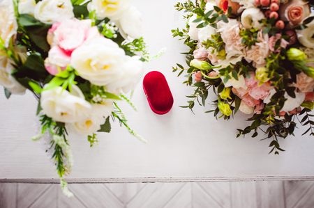 Photo image of a red velvet box with wedding rings of the bride and groom, on a white table, with a bridal bouquet of bridal flowersの写真素材