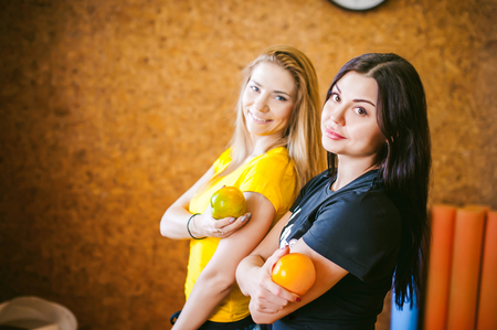 Two young athletic physique women in gym. Fitness girl with fruits, lifestyle in losing weight and diets, proper nutrition, exerciseの写真素材