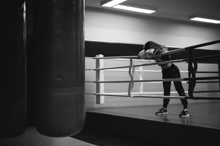 young woman in boxing gloves on a ring. girl looks tired, leaned on the ropes, after training in martial artsの写真素材