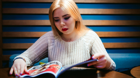 Picture of young lady sitting in cafe while reading magazine.の写真素材