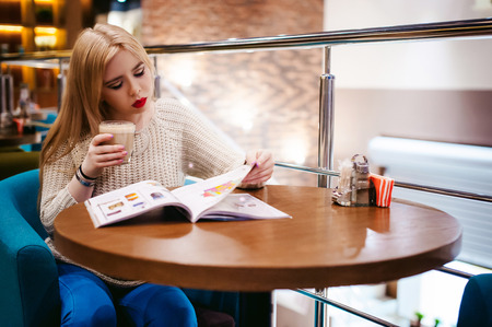 Picture of young lady sitting in cafe while reading magazine And drinks coffeeの写真素材