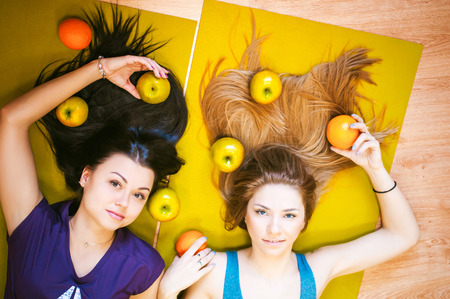 Two young athletic physique women in gym Lie on the floor on yoga mats. Fitness girl with fruits, lifestyle in losing weight and diets, proper nutrition, exerciseの写真素材