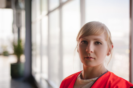 Portrait of a female employee in an orange robe vest in the working space of a production room, against a background of large windowsの写真素材
