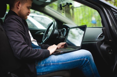 Professional man with a laptop in car tunes tuning control system, updating software, gaining access...