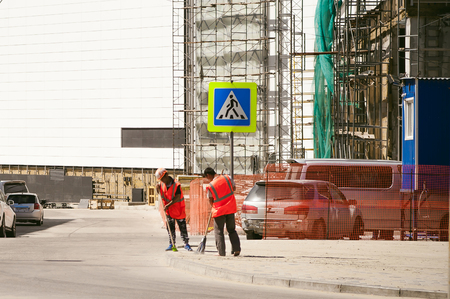 Worker in overalls sweeps sidewalk with a broom, on city street on warm summer dayの写真素材