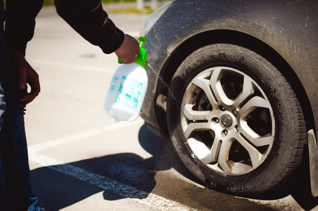 young bearded man washes his car's wheel rims, spraying water from spray, in street parkingの写真素材