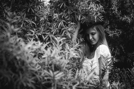 Black and white portrait of a young woman with a hat in bushesの写真素材