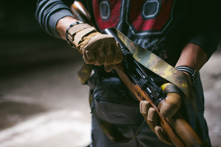 Athletic man in gray clothes with a carbine gun in his hand. Close-up of tactical gloves with weaponsの写真素材