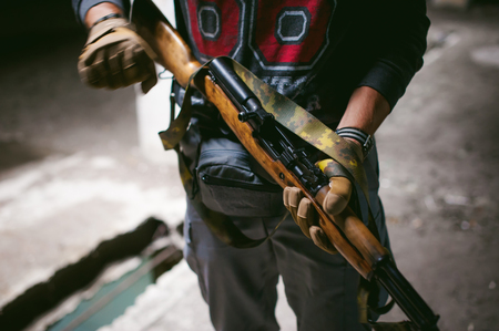 Athletic man in gray clothes with a carbine gun in his hand. Close-up of tactical gloves with weaponsの写真素材