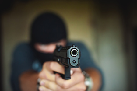 Athletic man in a balaclava, holds a pistol in his hand, is threatened with shooting, aimingの写真素材