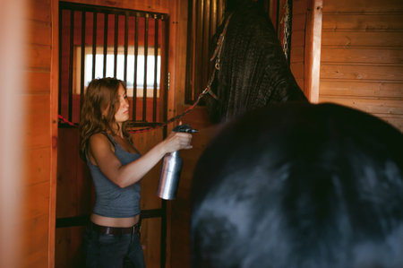 woman horseman cleans from dirt with brush Friesian horse in stables on farm, taking care of purebred petsの写真素材