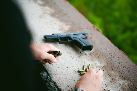 Man charges clip of pistol with bullets. Photo hands of paramilitary, reloading weapons. Preparation for shootingの写真素材