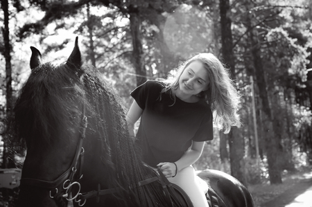 Emotional portrait of a horsewoman rider woman, astride, in love with horses, black Friesian stallion thoroughbred pet, outdoorsの写真素材