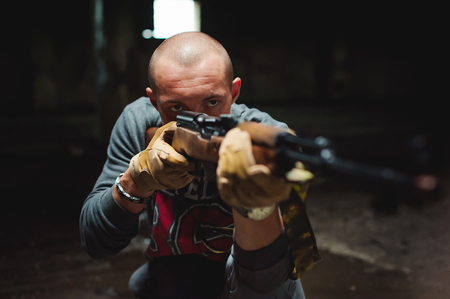 Athletic man in gray clothes with a carbine gun in his hand. Close-up of tactical gloves with weapons. Aiming at distance, front viewの写真素材