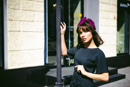 Beautiful woman in a dark stylish dress strolls along the street, near boutiques. Portrait of a fashionable girlの写真素材