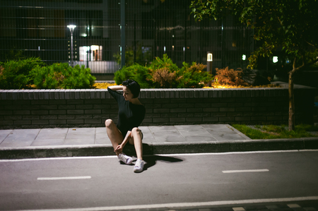 young woman with beautiful feet dressed in white sneakers and black dress, against a backdrop of urban landscapes. Street fashion. night dark styleの写真素材