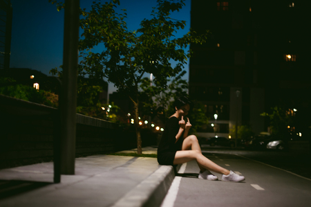 young woman with beautiful feet dressed in white sneakers and black dress, against a backdrop of urban landscapes. Street fashion. night dark styleの写真素材
