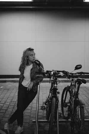 young beautiful woman in jeans clothes in parking of shopping center. portrait of a girl with freckles on her face near the bicycleの写真素材