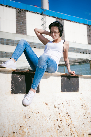 young woman dressed in white sneakers, a T-shirt and blue jeans, against the backdrop of cityscapes. Street fashionの写真素材