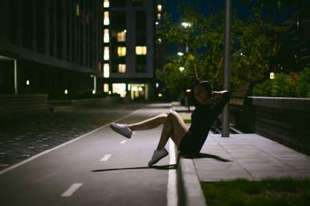 young woman with beautiful feet dressed in white sneakers and black dress, against a backdrop of urban landscapes. Street fashion. night dark styleの写真素材