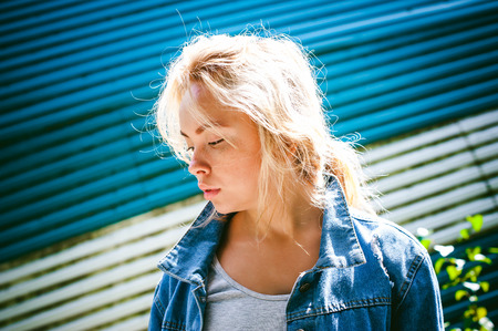 young woman in jeans clothes outdoors. portrait of a girl with freckles on her face, against the background of a metal striped fence, on a sunny summer dayの写真素材