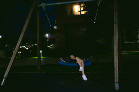 young woman with beautiful feet dressed in white sneakers and black dress lies in a swing in the yard, against a backdrop of urban landscapes. Street fashion. night dark styleの写真素材