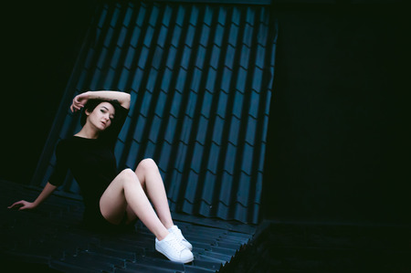 young woman with beautiful feet dressed in white sneakers and black dress, against a backdrop of urban landscapes. Street fashion. dark styleの写真素材
