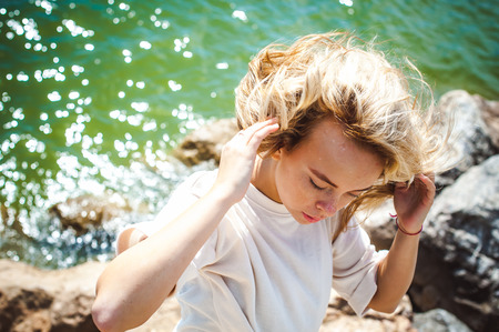 Portrait young woman on stones near sea. Beautiful girl is resting on coast, enjoying outdoor recreation.の写真素材