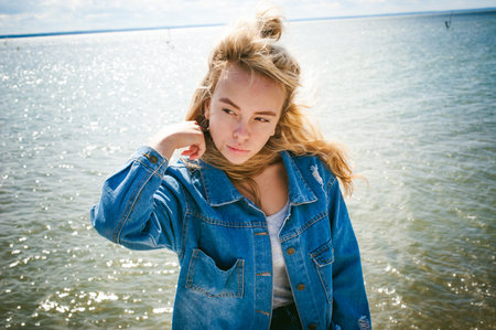 young beautiful woman in jeans clothes outdoors. portrait of a girl with freckles on her face, stylish girl on sea beach, on a sunny summer autumn day.の写真素材