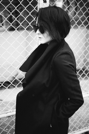emotional fashionable portrait of a young brunette woman in black clothes, jeans T-shirt, coat and sunglasses, in a Gothic style sad mood.の写真素材