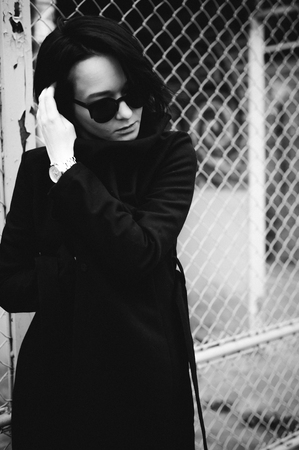 emotional fashionable portrait of a young brunette woman in black clothes, jeans T-shirt, coat and sunglasses, in a Gothic style sad mood.の写真素材