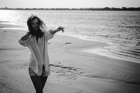lovely young woman with curly hair, the romance of youth, a journey walk on a warm summer sunny day on a sandy beach with waterの写真素材