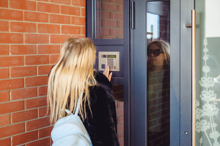 young blond woman in a fur coat, dials the code on the doorphone panel, presses  buttons with her...