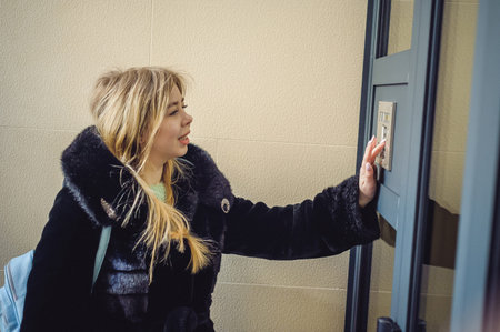 young blond woman in a fur coat, dials the code on the doorphone panel, presses  buttons with her...