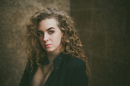 city portrait of a young woman with curly hair dressed in a black coatの写真素材