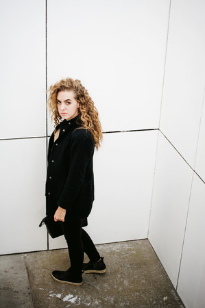 city portrait of a young woman with curly hair dressed in a black coatの写真素材