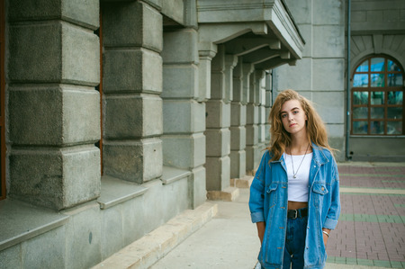 street portrait of a young attractive emotional girl with curly slips dressed in a trendy blue jeans suit on a style walking in the open airの写真素材