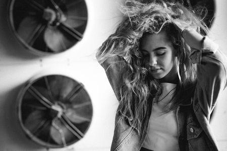 street portrait of a young attractive emotional girl with curly hair dressed in a trendy denim suit on the style. against the background of air conditioner ventilator systems. the wind in her hairの写真素材