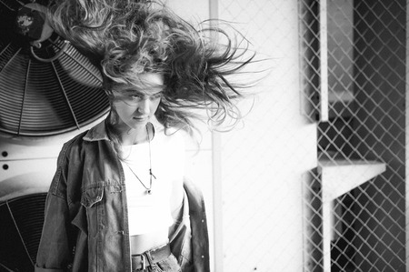 street portrait of a young attractive emotional girl with curly hair dressed in a trendy denim suit on the style. against the background of air conditioner ventilator systems. the wind in her hairの写真素材