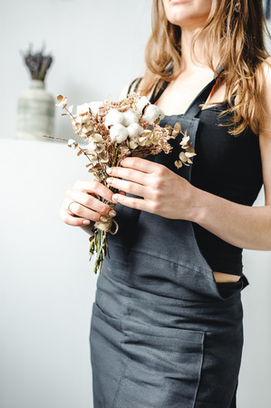 woman artist in dark clothes holding a bouquet plant cottonの写真素材