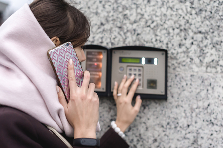 brunette woman calls into the intercom on the street, autumn day in warm clothesの写真素材