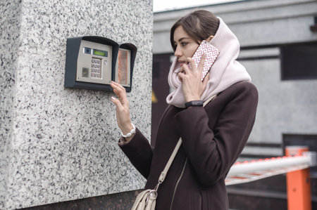 brunette woman calls into the intercom on the street, autumn day in warm clothes