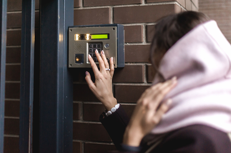 brunette woman calls into the intercom on the street, autumn day in warm clothesの写真素材
