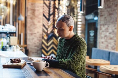 Russia, Novosibirsk - September 01, 2018: bald woman with amazing tattoo on her head. reading book over cup of warming coffee drink sitting in cafeのeditorial素材