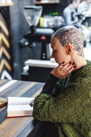 Russia, Novosibirsk - September 01, 2018: bald woman with amazing tattoo on her head. reading book...