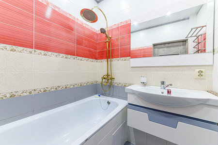 Interior of a bathroom with red tiles, white bathtub and shower