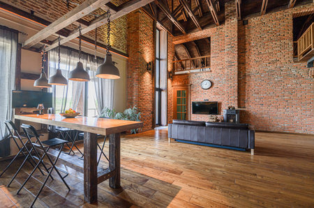 spacious loft with exposed brick walls, wooden floors, and a high ceiling. A long table with industrial-style lamps dominates the foreground